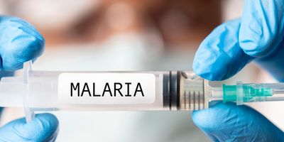 Gloved hands hold a syringe labeled Malaria to indicate a malaria vaccine.