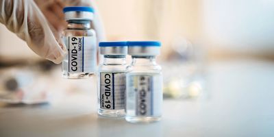 A gloved hand picks a vial of COVID-19 vaccine from a series of three vials.