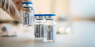 A gloved hand picks a vial of COVID-19 vaccine from a series of three vials.