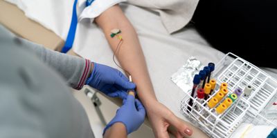 A nurse draws blood from a patient and fills several blood vacutainers that are arranged in a stand.