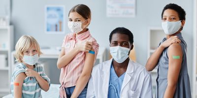 A clinician with a group of children showing their shoulder patches after getting vaccinated.