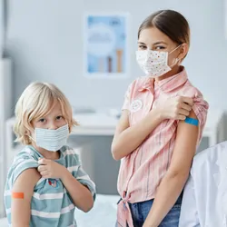 A clinician with a group of children showing their shoulder patches after getting vaccinated.