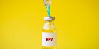 HPV vaccine vial with a syringe in it to load against a yellow background.