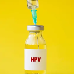 HPV vaccine vial with a syringe in it to load against a yellow background.