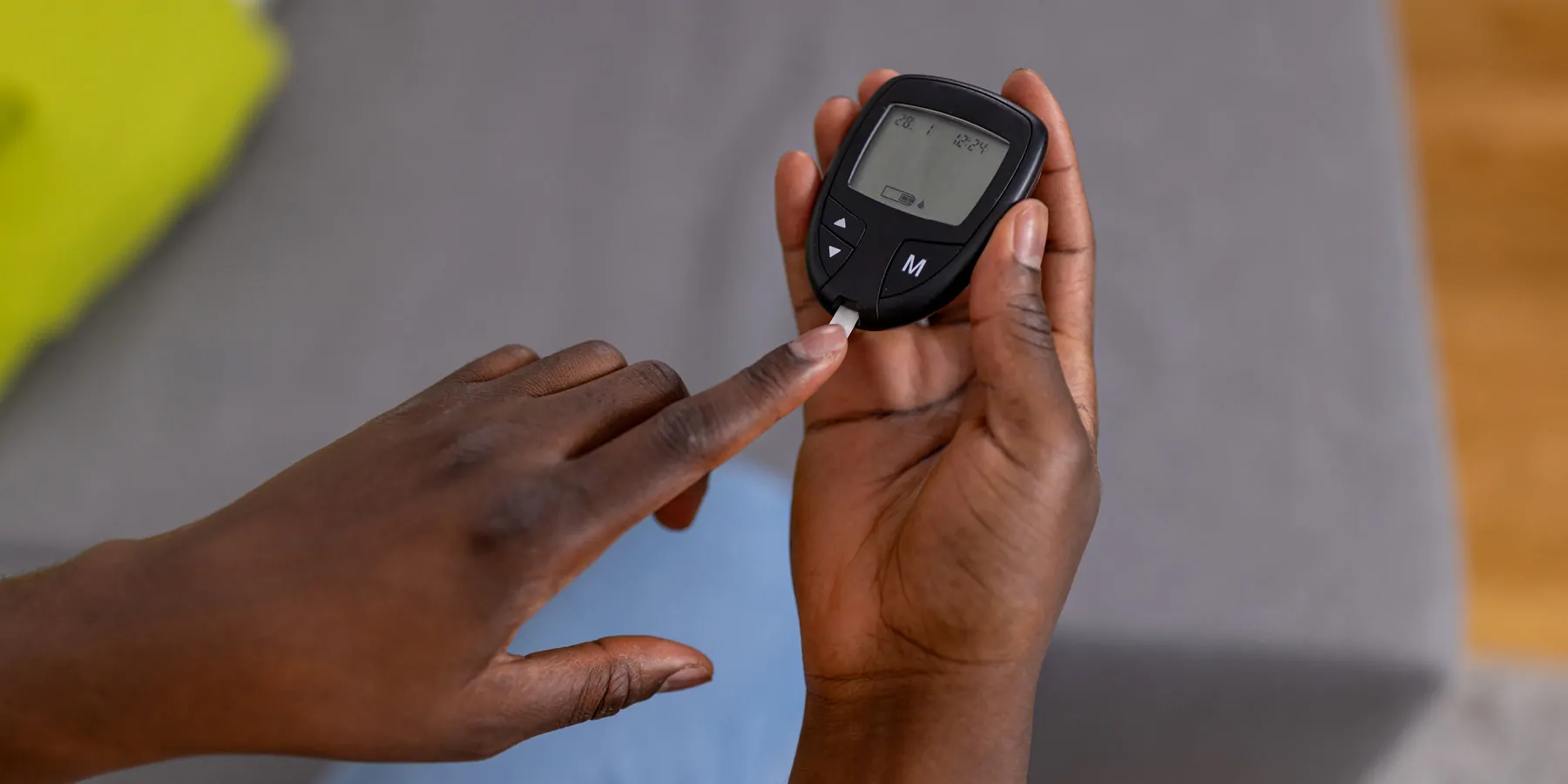 A young Black person measures blood sugar using a glucose monitor and strips.