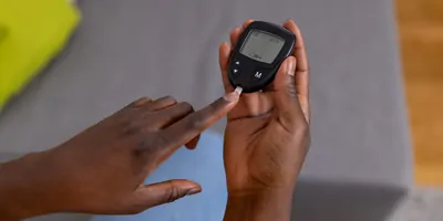 A young Black person measures blood sugar using a glucose monitor and strips.