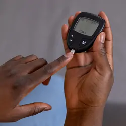 A young Black person measures blood sugar using a glucose monitor and strips.