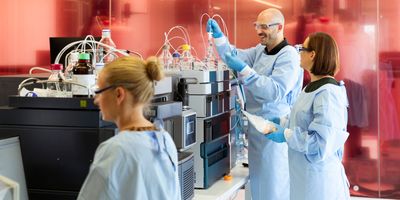 Female and male scientists in PPE working on mass spectrometers in a laboratory.