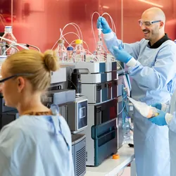 Female and male scientists in PPE working on mass spectrometers in a laboratory.