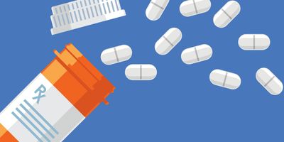 Pills fallen out of a prescription drug bottle on a blue background.