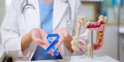 Close-up of female clinician holding a blue ribbon with both hands in front of her chest beside colon model on the table.