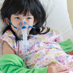 A sick little girl has a nebulizer mask on for respiratory treatment.