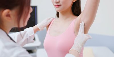 A female clinician examines the lymph nodes in a woman's armpit.