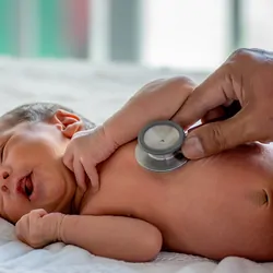 A clinician checks a newborn baby with a stethoscope in a hospital.