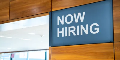 Photo of a business with a sign on the wall that reads, Now Hiring.