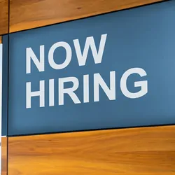Photo of a business with a sign on the wall that reads, Now Hiring.