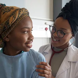 A female clinician checks a young girl's heartbeat with a stethoscope in a hospital ward.