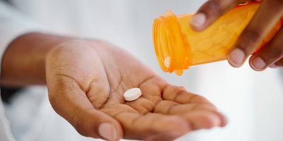 Close-up of a person taking one tablet from a bottle of prescription drugs.