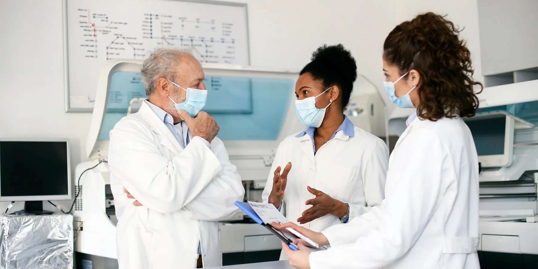A team of scientists, one White male, one African female, and one Mixed-race female, discuss research findings in a lab.