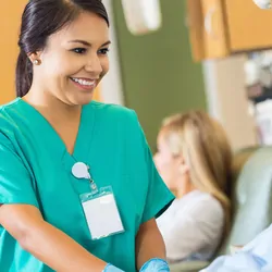  A smiling female nurse comforting a male patient lying on a hospital bed.
