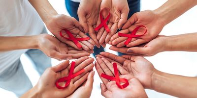 A group of hands holding red ribbons in support of HIV/AIDS awareness.