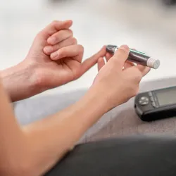 A person uses a glucometer to test glucose levels in blood from a lancet-pricked finger.