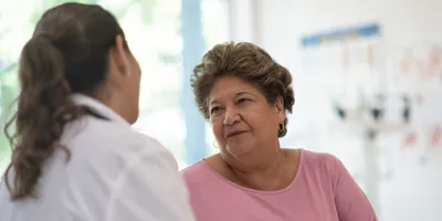 A senior Hispanic or mixed-race woman speaks to a female doctor.