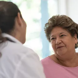 A senior Hispanic or mixed-race woman speaks to a female doctor.