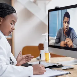 Shot of a young female clinician writing notes during a video call with a male patient.