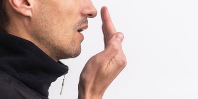 A young man checks his breath with his hand cupped in front of his mouth.