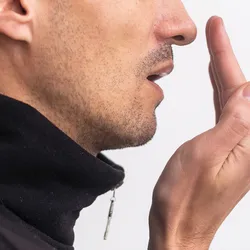 A young man checks his breath with his hand cupped in front of his mouth.