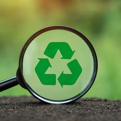 Recycling symbol in magnifying glass on nature background.