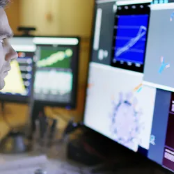 Stock photo of a young man working a large monitor displaying a variety of data & illustrations of viruses and antibodies