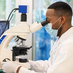 A clinical pathologist at a hub laboratory examines a sample using a microscope.