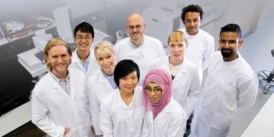 A group of clinical lab professionals wearing white lab coats post together for a photo in the lab.