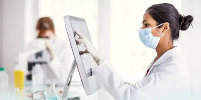 Photo of a clinical lab professional wearing PPE and using a clinical informatics software at a computer in the lab.