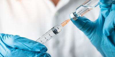 A pair of gloved hands load a clear, colorless liquid from a vial into a syringe.