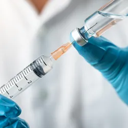 A pair of gloved hands load a clear, colorless liquid from a vial into a syringe.