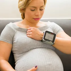 Expectant mother checks her blood pressure with a wrist heart rate monitor at home.