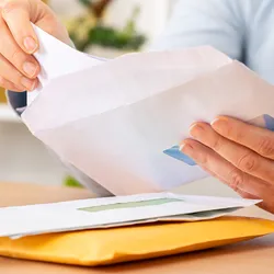 Close-up of a person taking a letter out from an envelope on a desk at home or office.