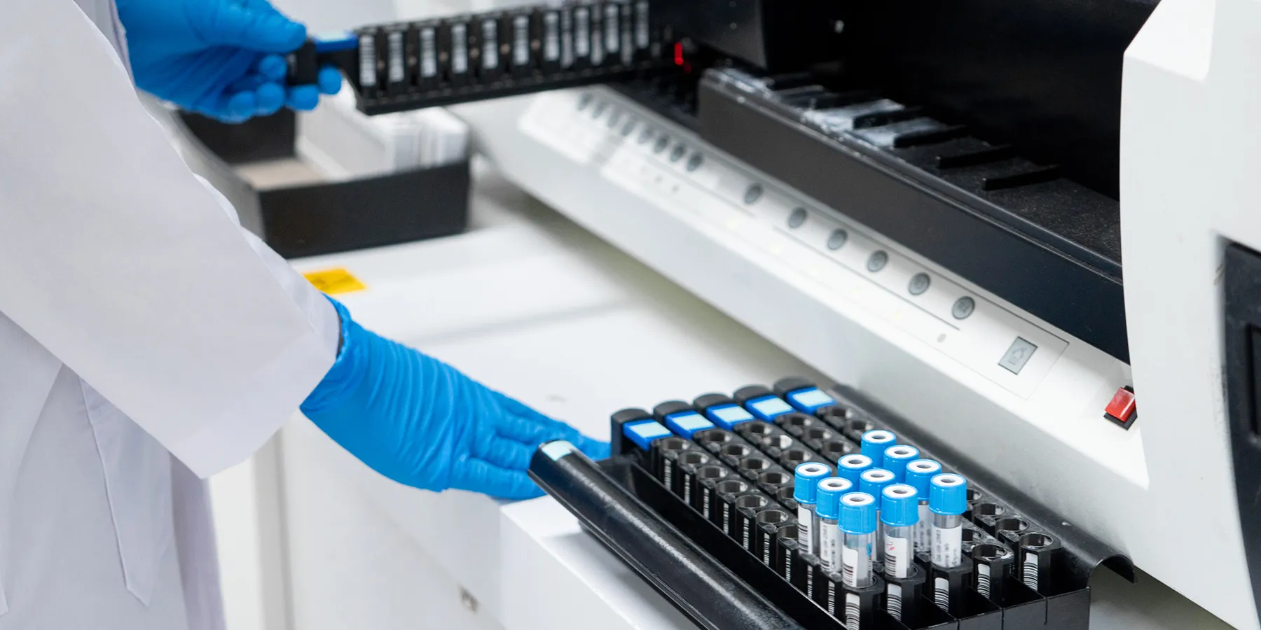 A gloved hand loads prepped samples into a liquid chromatography instrument. 