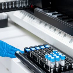 A gloved hand loads prepped samples into a liquid chromatography instrument. 