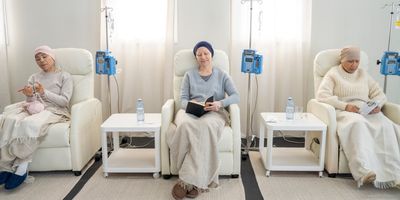 Three women with head scarves sit in individual chairs as they receive intravenous chemotherapy.