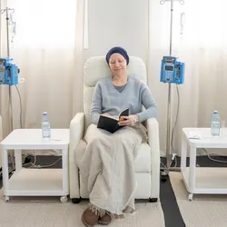 Three women with head scarves sit in individual chairs as they receive intravenous chemotherapy.