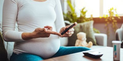 A pregnant woman hands using a lancet on her finger to check her blood sugar levels with a glucose meter.