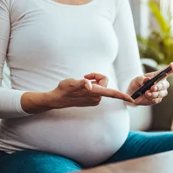 A pregnant woman hands using a lancet on her finger to check her blood sugar levels with a glucose meter.