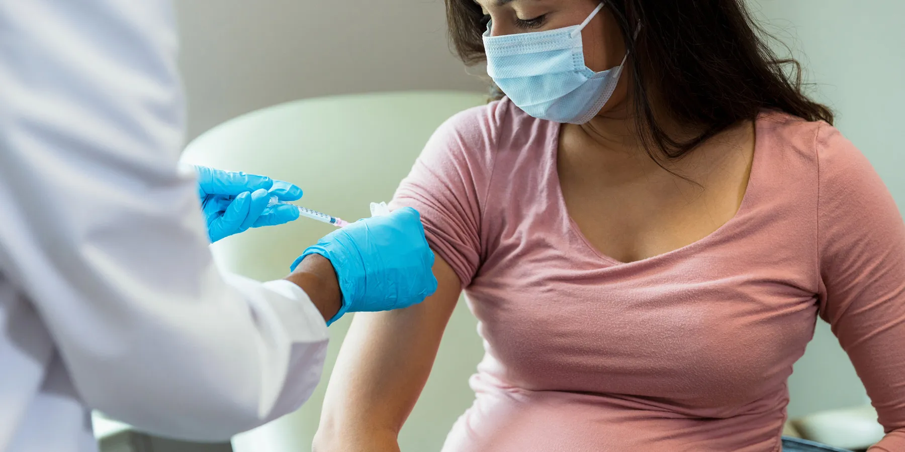 A clinician administers a COVID-19 vaccine to a masked pregnant woman.