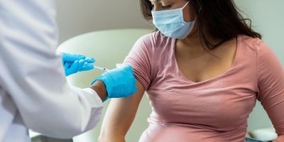 A clinician administers a COVID-19 vaccine to a masked pregnant woman.