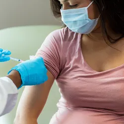 A clinician administers a COVID-19 vaccine to a masked pregnant woman.