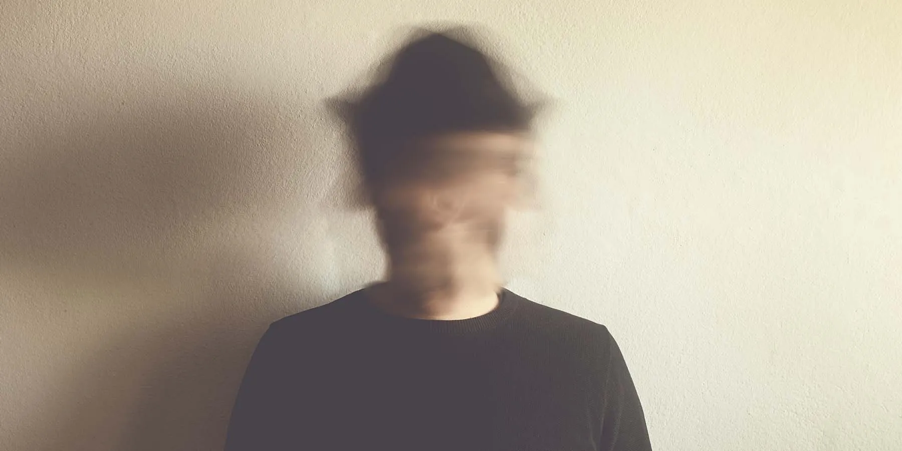 A blurred face of a man wearing a black hat and black shirt, indicating psychiatric instability.